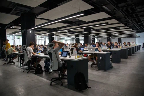 A photo of an office with multiple computers. People are working at the computers. A photo of an office with multiple computers. People are working at the computers.