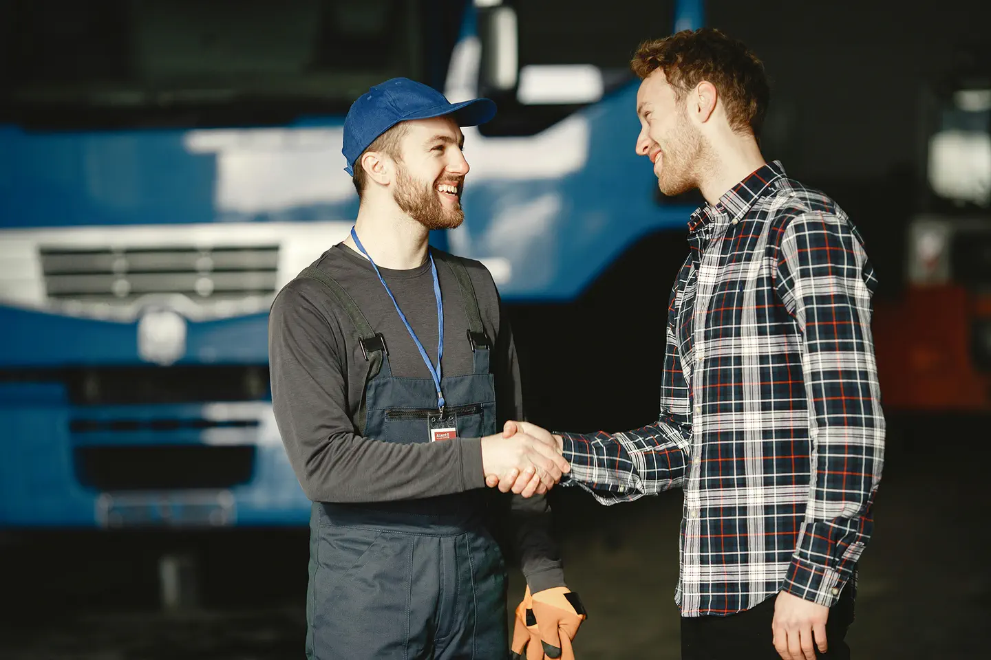 A photo of two people shaking hands in a warehouse. A blue truck is in the background.