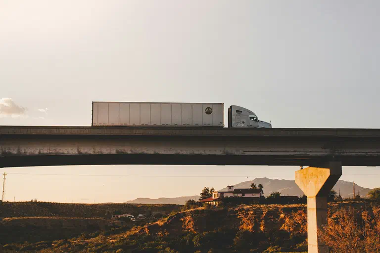 A photograph of a dry van semi truck driving over a bridge. A photograph of a dry van semi truck driving over a bridge.