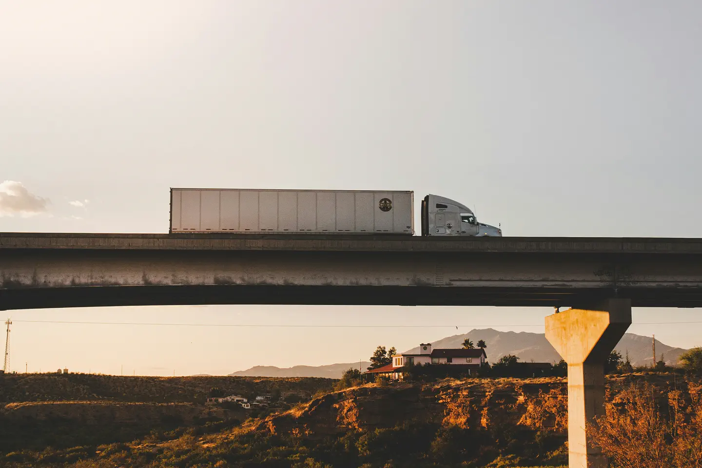 A photograph of a dry van semi truck driving over a bridge.